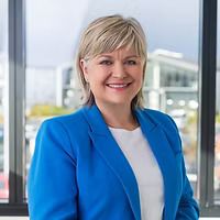 Woman in a blue blazer smiles in front of a window.