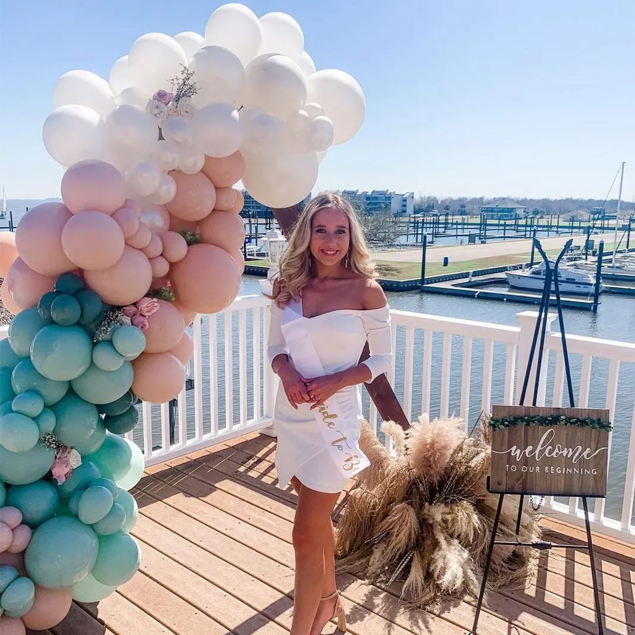 Woman in white dress stands by a balloon arch, a 