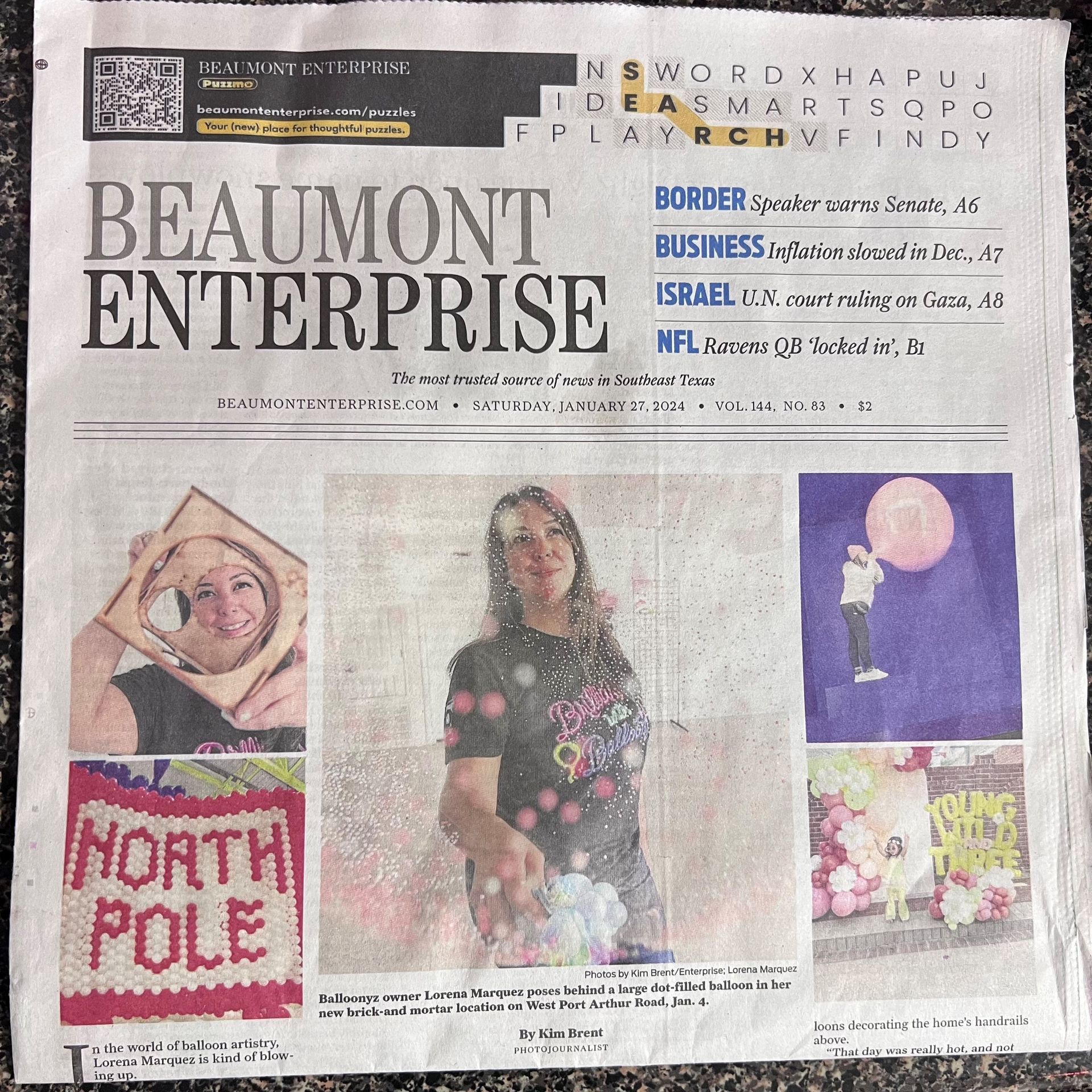 Two people wearing masks sit on an orange couch in front of a 