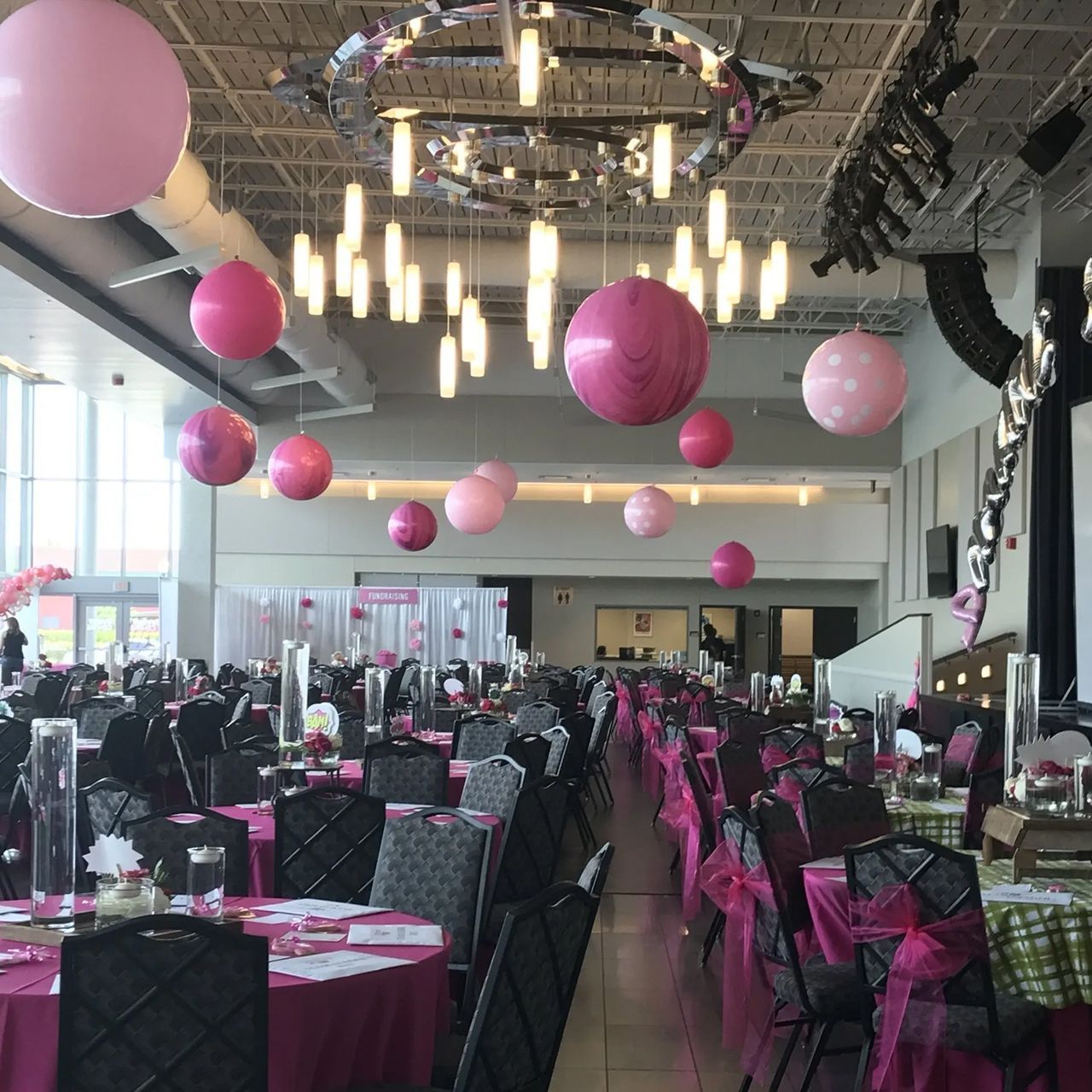 Event hall decorated with pink balloons, tables, and chair sashes.