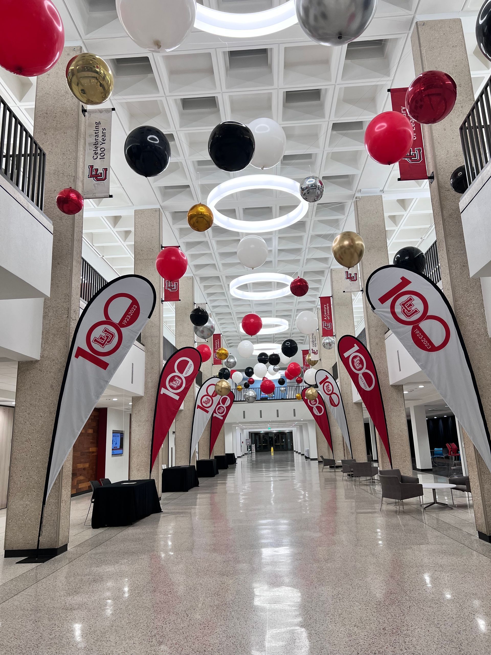 Long hallway decorated with balloons and banners, celebrating a centennial.
