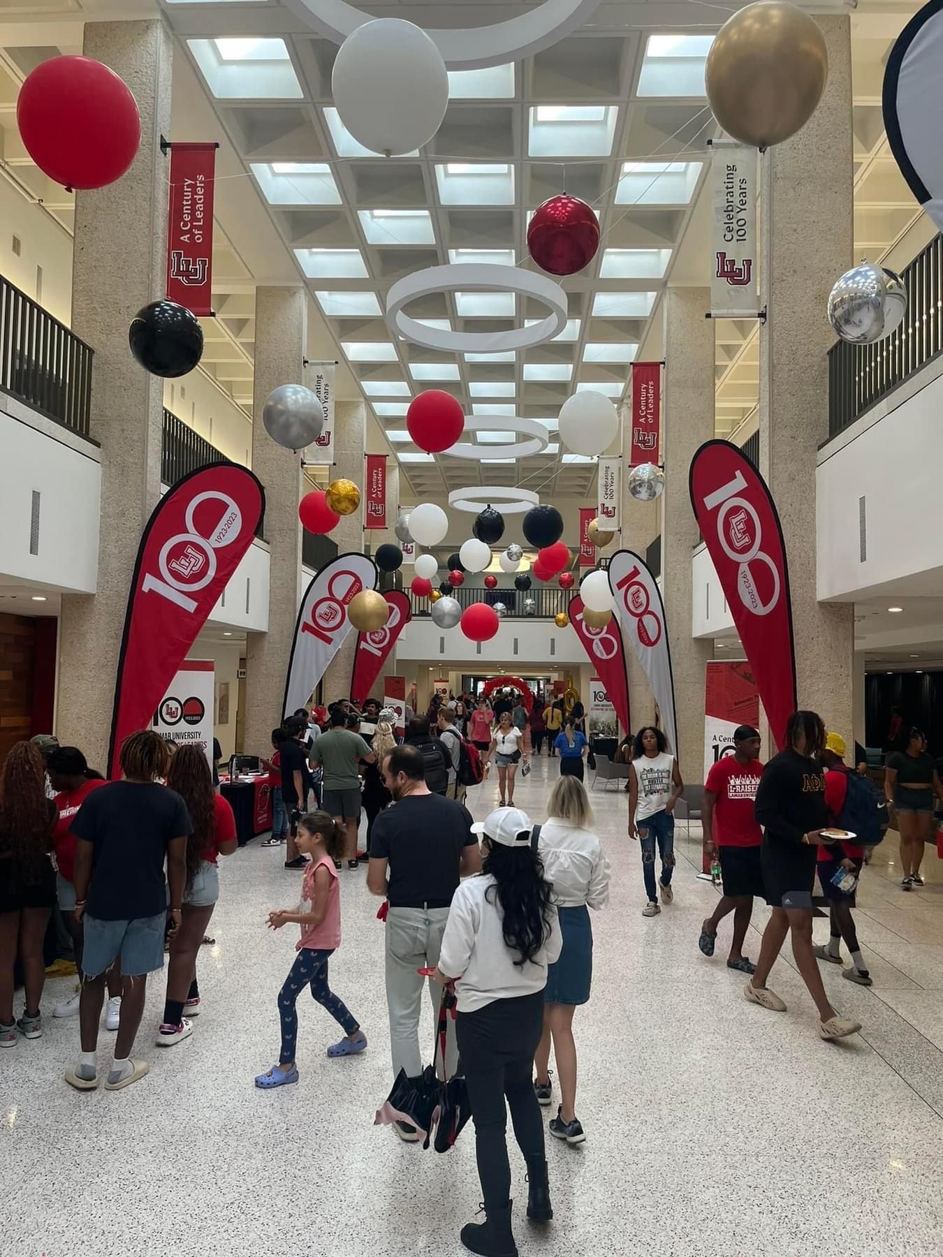 Hallway with balloons, banners, and people at an event. Red, black, and white decorations.