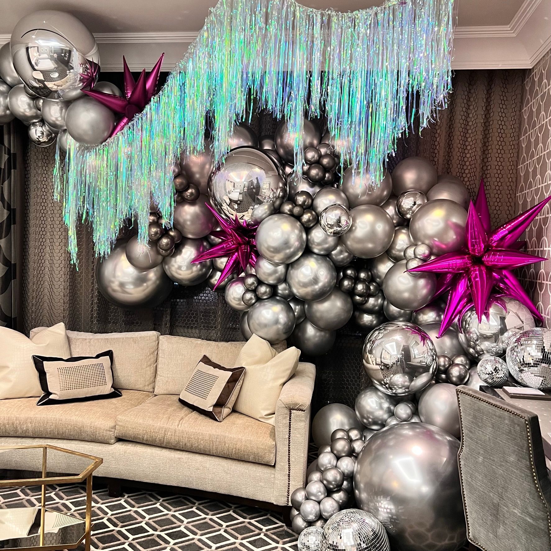 Silver balloons, fuchsia stars, and disco balls decorate a room with a fringed backdrop and couch. Silver balloons, fuchsia stars, and disco balls decorate a room with a fringed backdrop and couch.