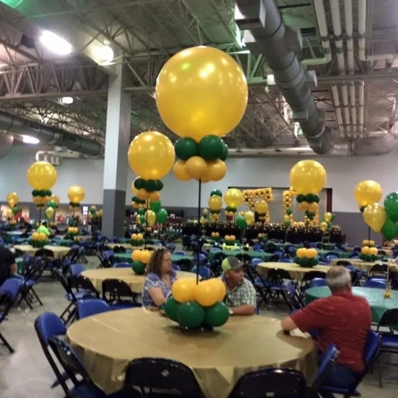 Event hall with round tables decorated with gold and green balloons. People seated at tables. Event hall with round tables decorated with gold and green balloons. People seated at tables.