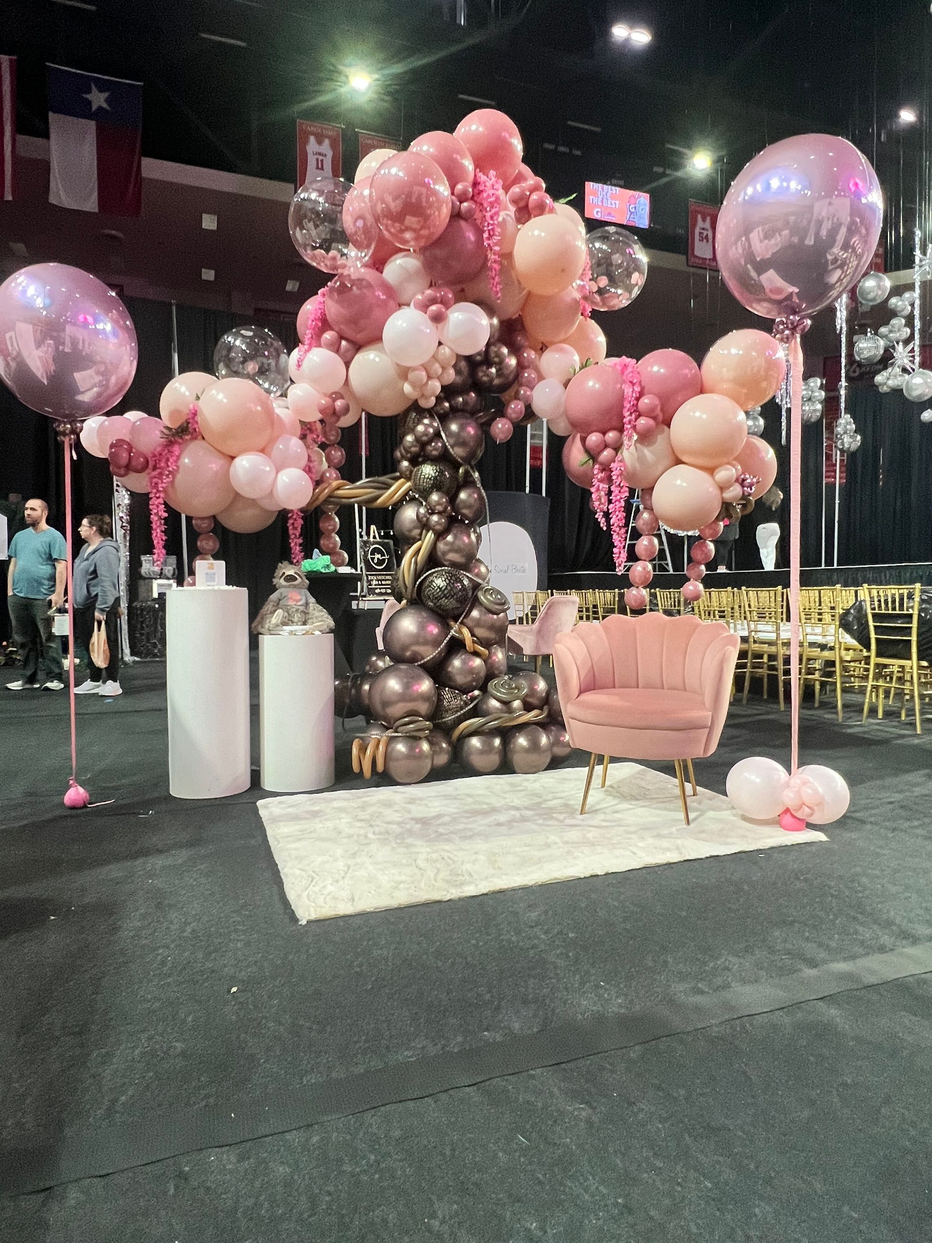 Pink balloon arch with armchair on rug. Event setting with flags in background.