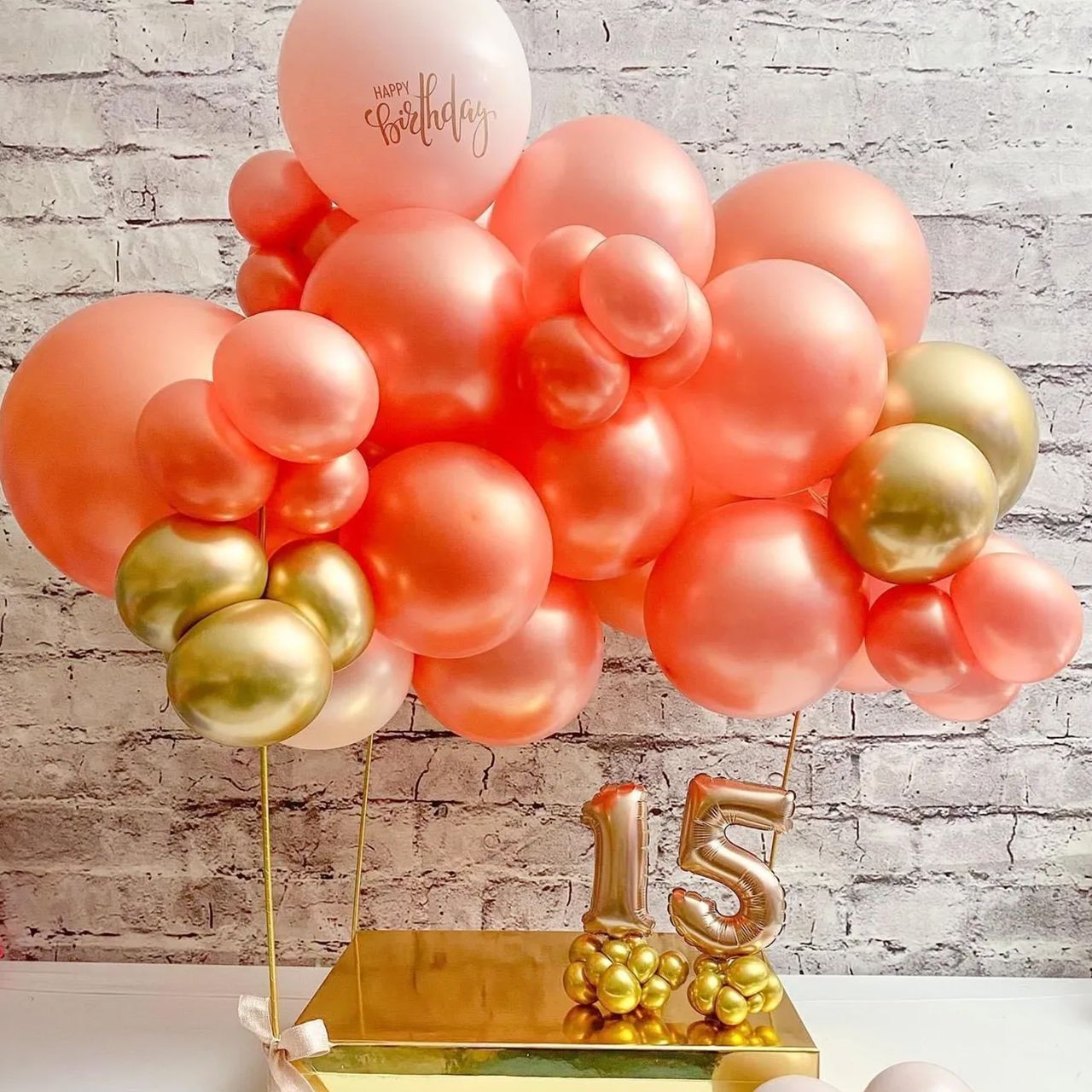 Pink, gold, and white balloons form a festive display above a gold base with 