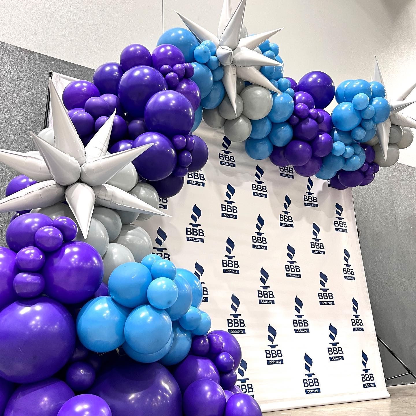 Balloon arch with starburst accents in shades of purple, blue, and silver in front of a backdrop.