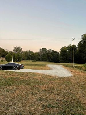 A black car is parked on the side of a dirt road in a field.