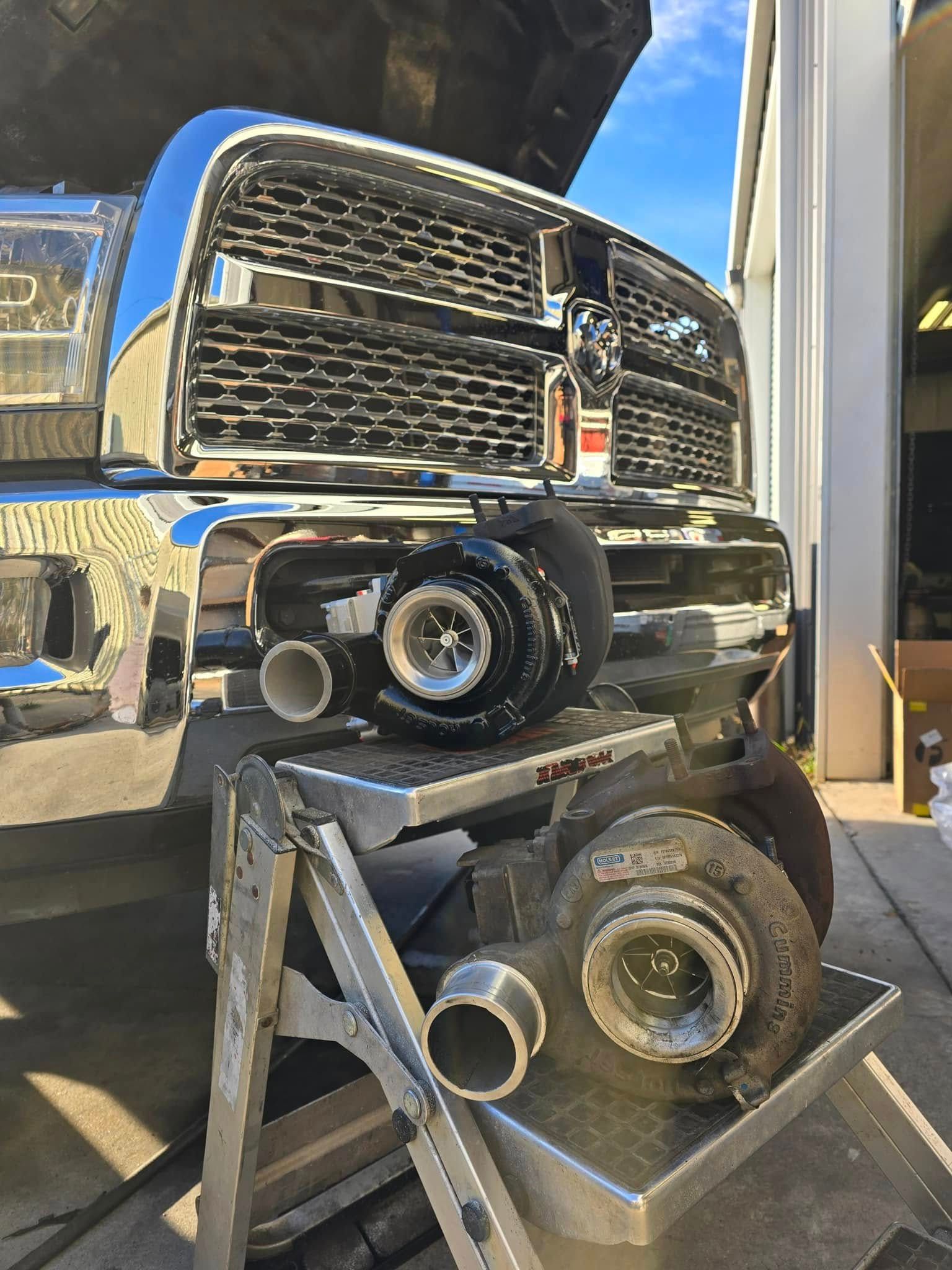 A ram truck with the hood up is sitting on a ladder.