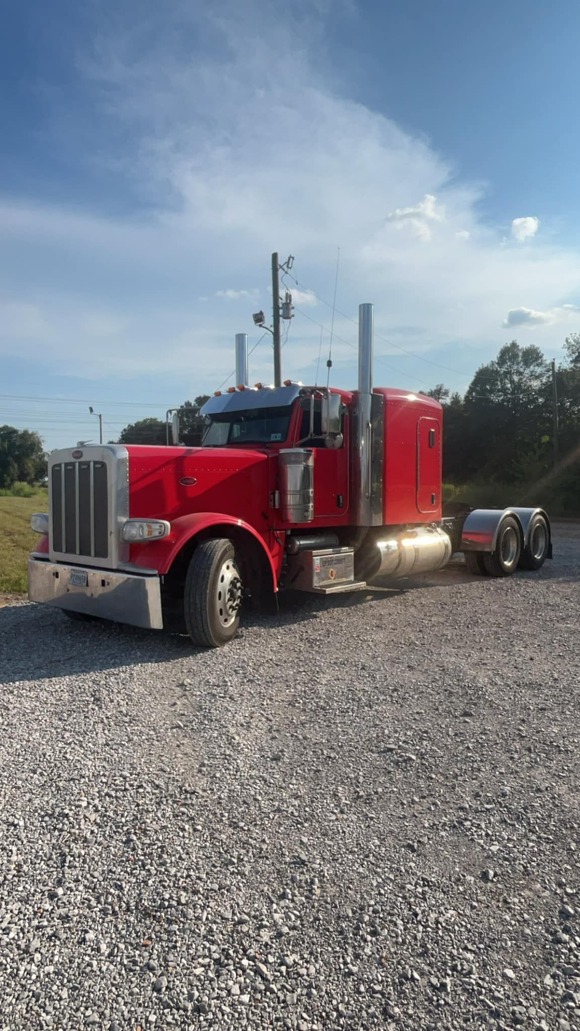 A red semi truck is parked in a gravel lot.