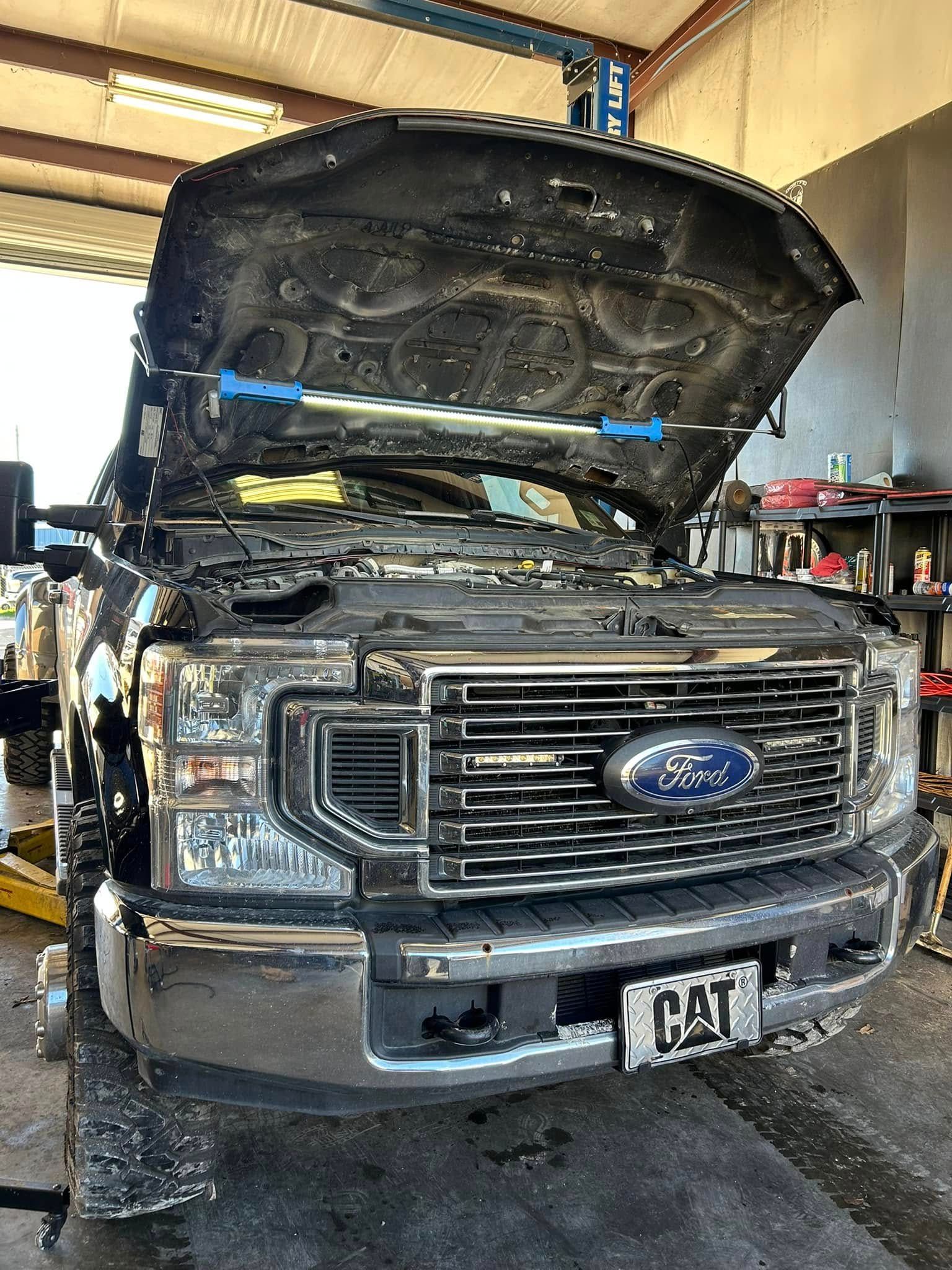 A ford truck is sitting in a garage with the hood open.