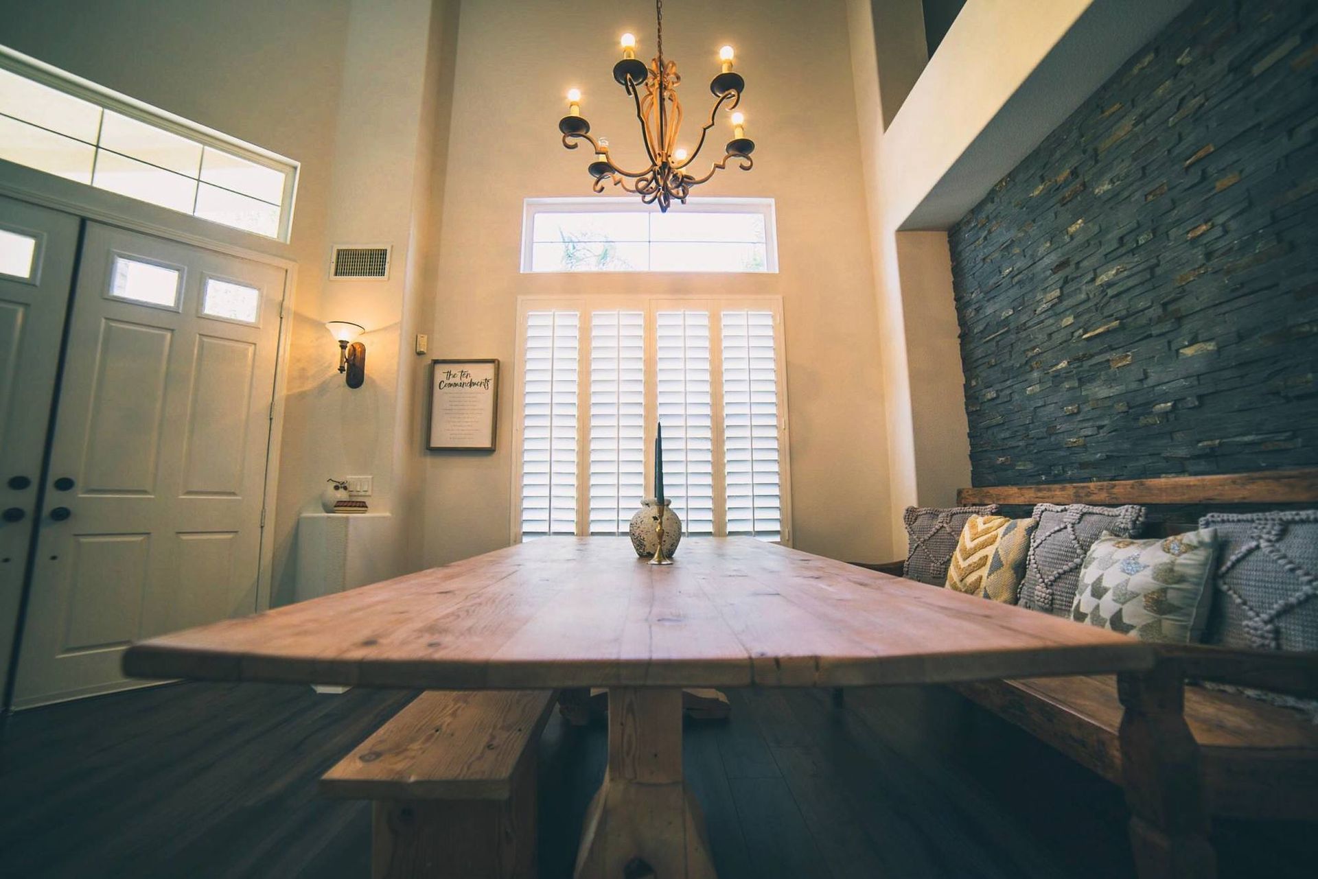 A dining room with a long wooden table and benches and a chandelier.