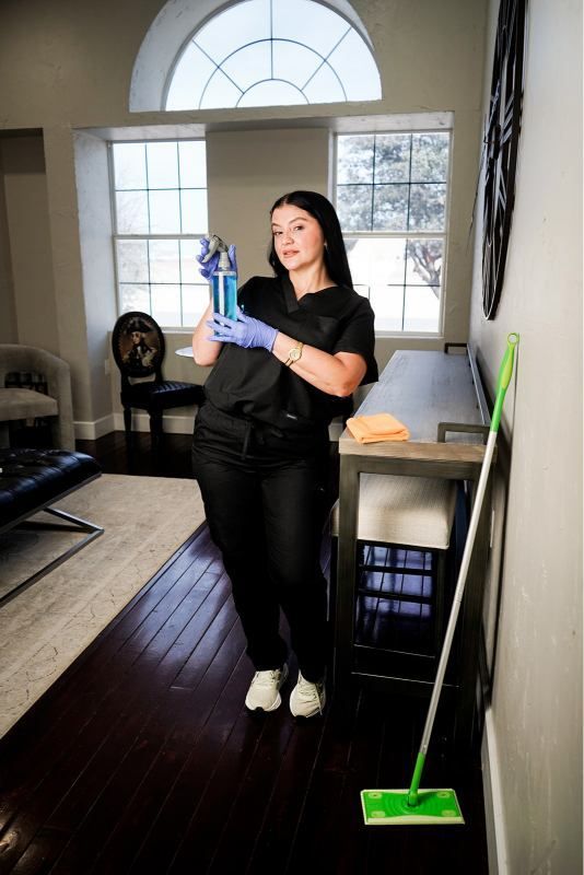 Person cleaning a bright room with a mop and spray bottle, wearing gloves and black clothes.