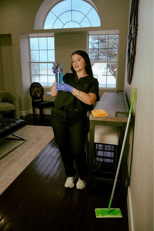Person cleaning a living room with a green mop, wearing gloves and holding a spray bottle