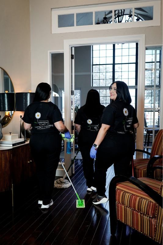 Three cleaning staff vacuum a room with dark wood floors and a large window.