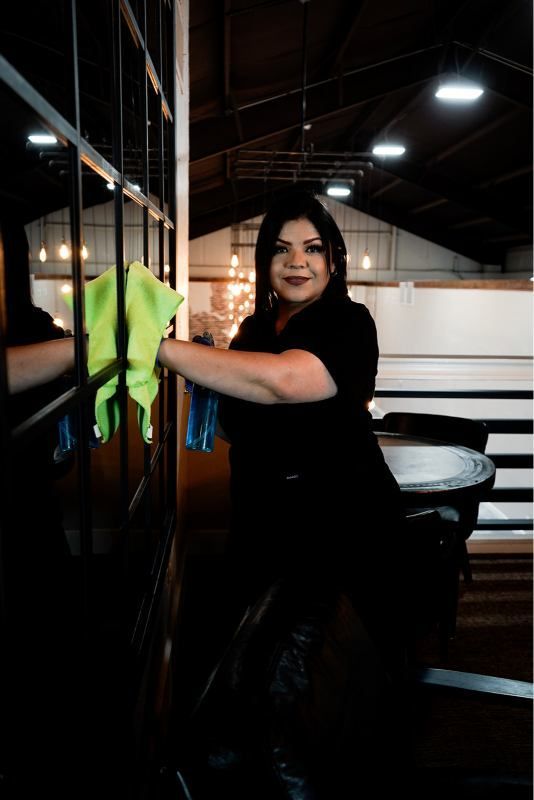 Person cleaning a mirror with a neon green cloth in a dim restaurant or bar interior