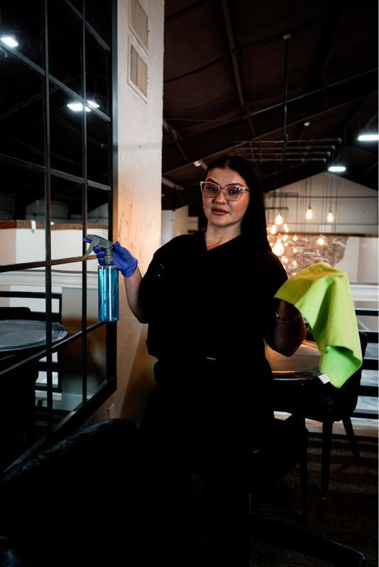 Person in dark clothing and sunglasses stands indoors near stairs, holding a blue item.