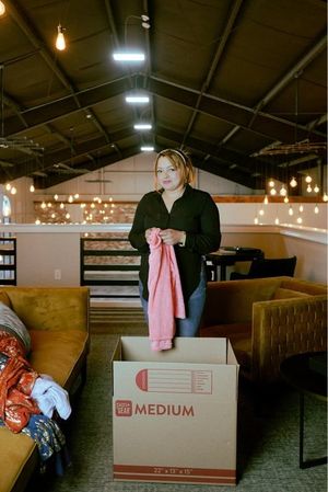 Person taping a cardboard box during a move, with stacked boxes and a small plant nearby