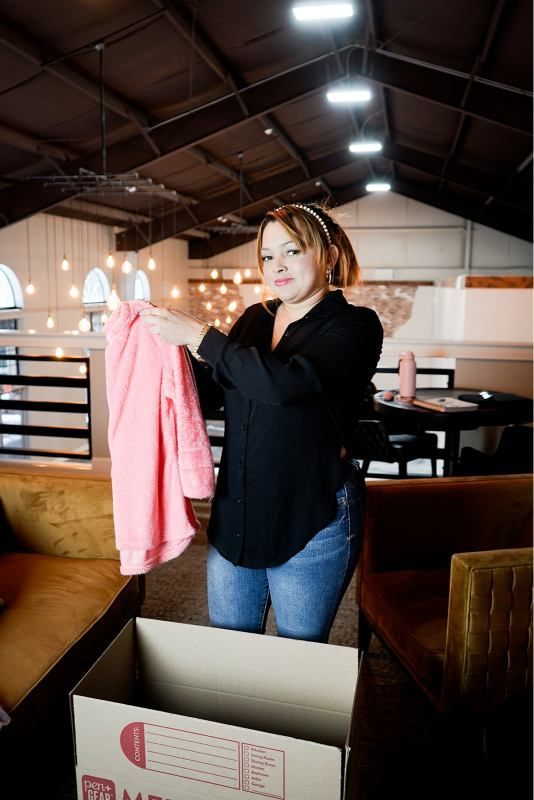 Woman in a black top holding a pink sweater inside a warehouse-like store.