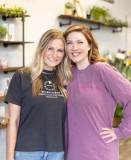 two women standing in front of flowers