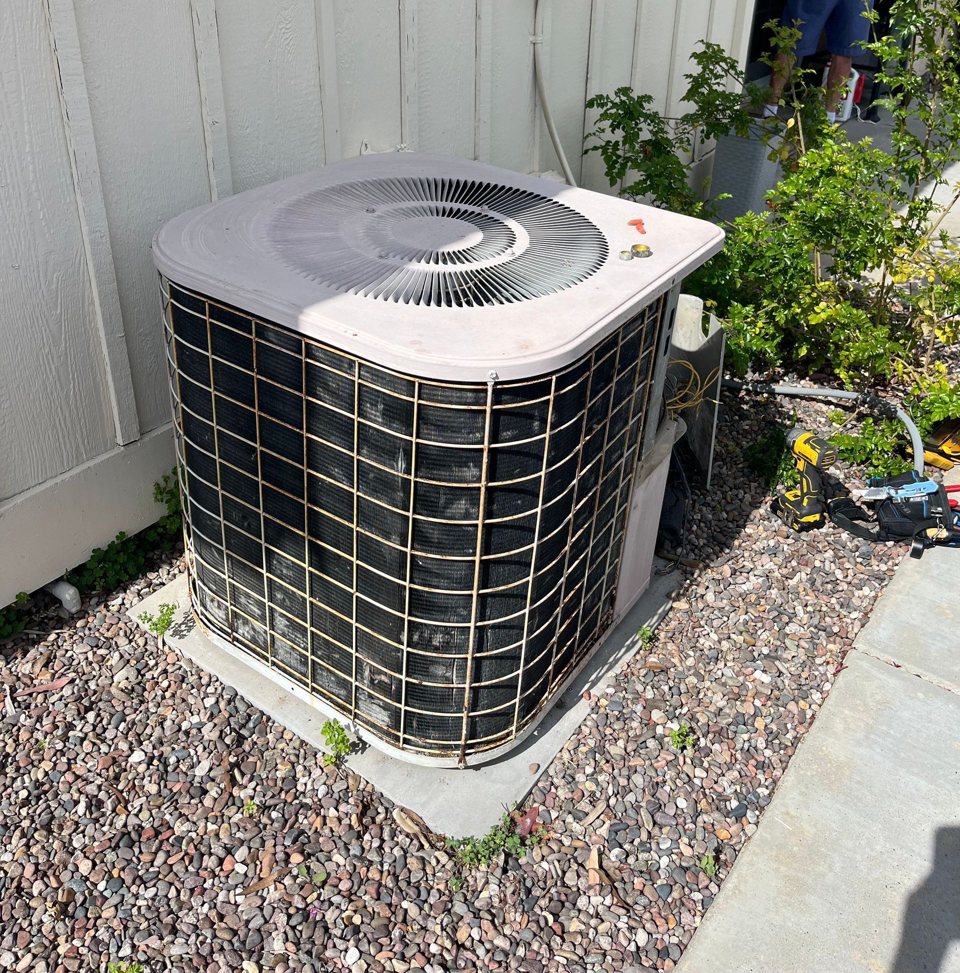 A man is standing next to an air conditioner holding a tool.