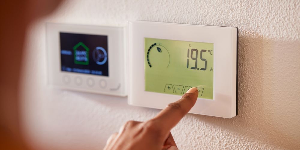 A person is adjusting a digital thermostat on a wall.