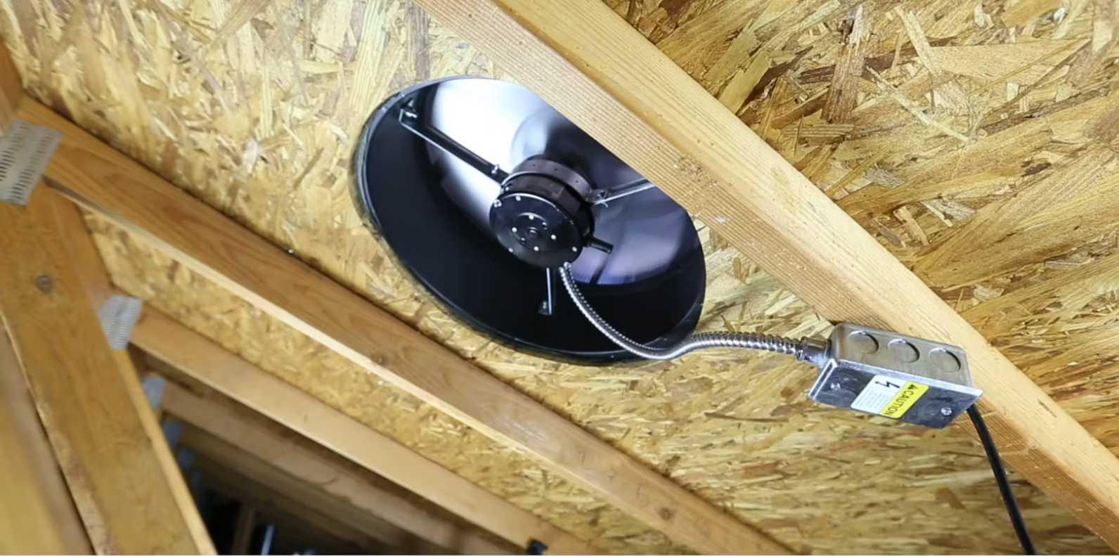 A fan is hanging from the ceiling of an attic.