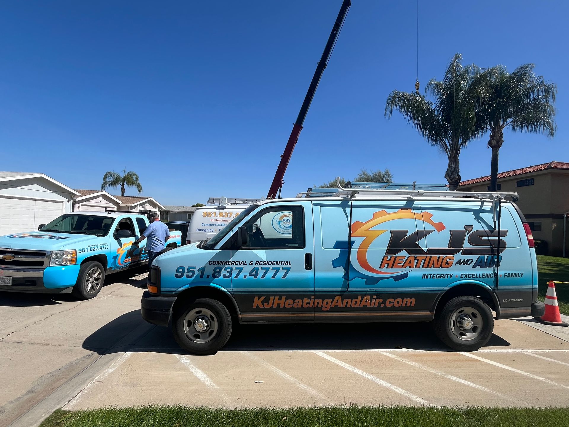 Two HVAC vans parked on pavement near a house on a sunny day, with a man standing near them.