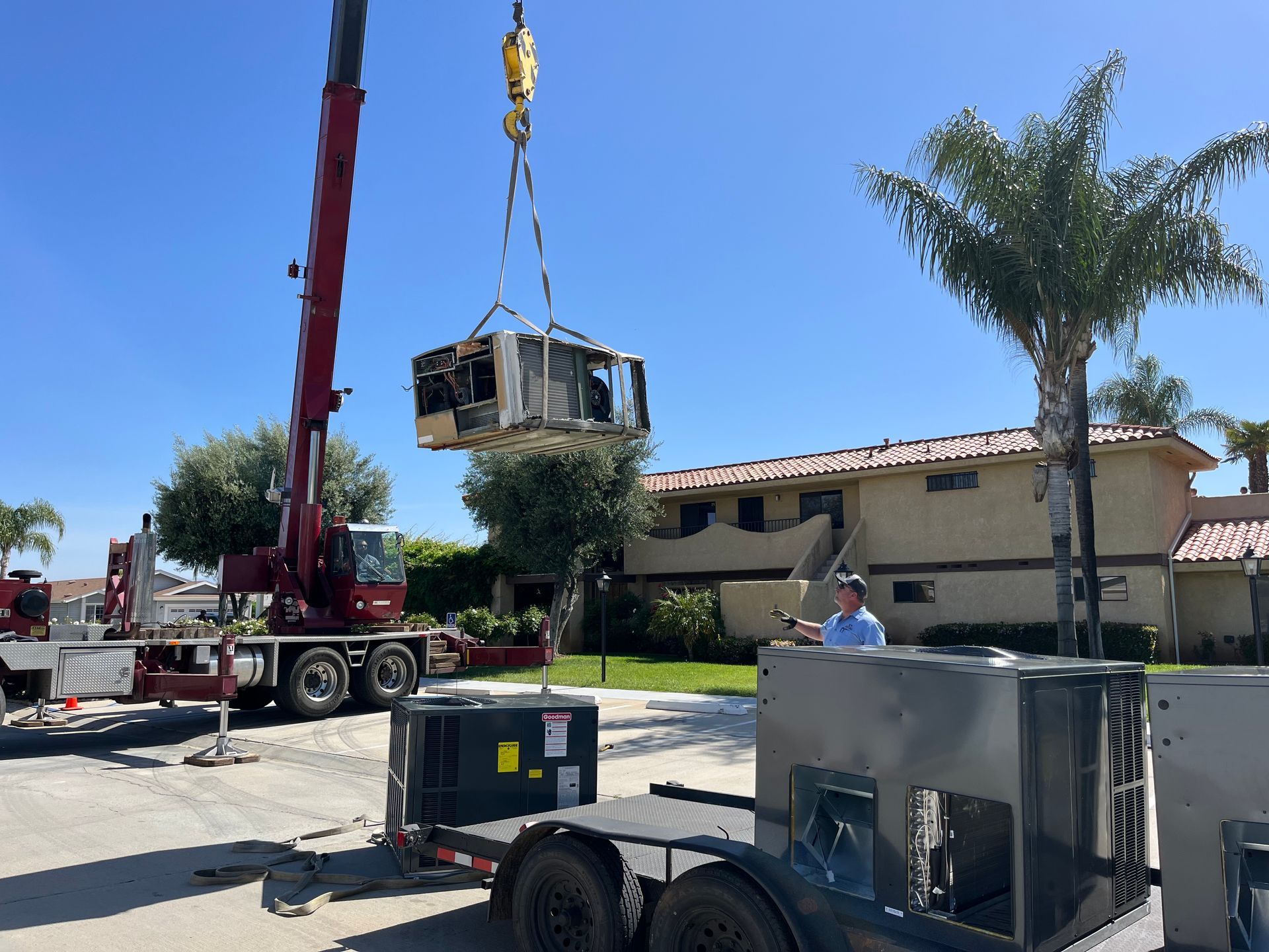 A crane lifting an HVAC unit near a residential building on a sunny day.