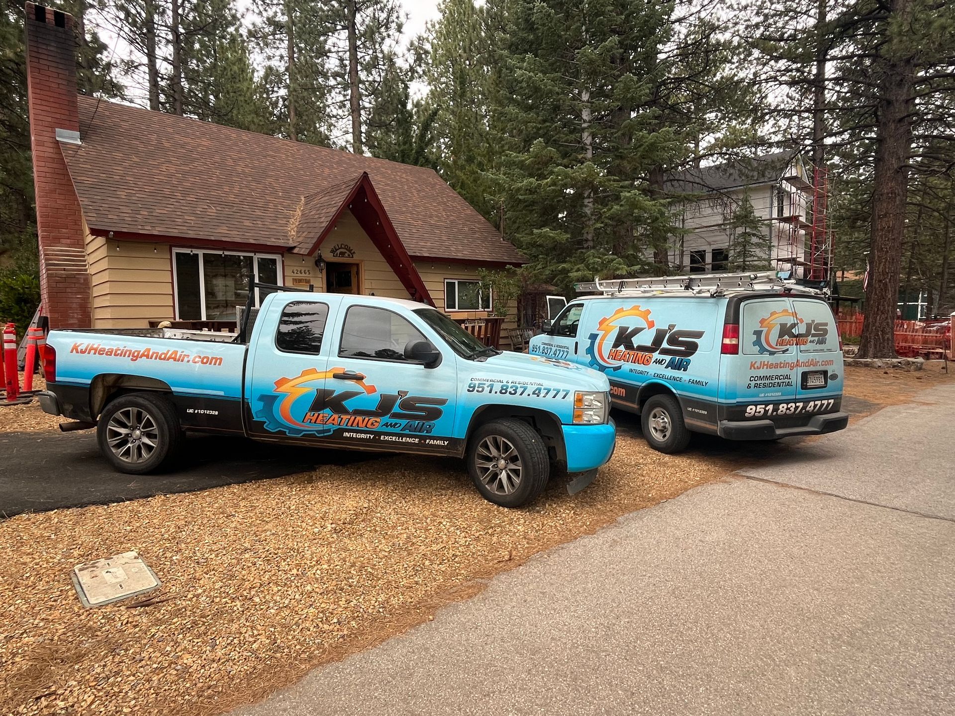 Two KJS plumbing vehicles parked in front of a house, featuring blue and black graphics.