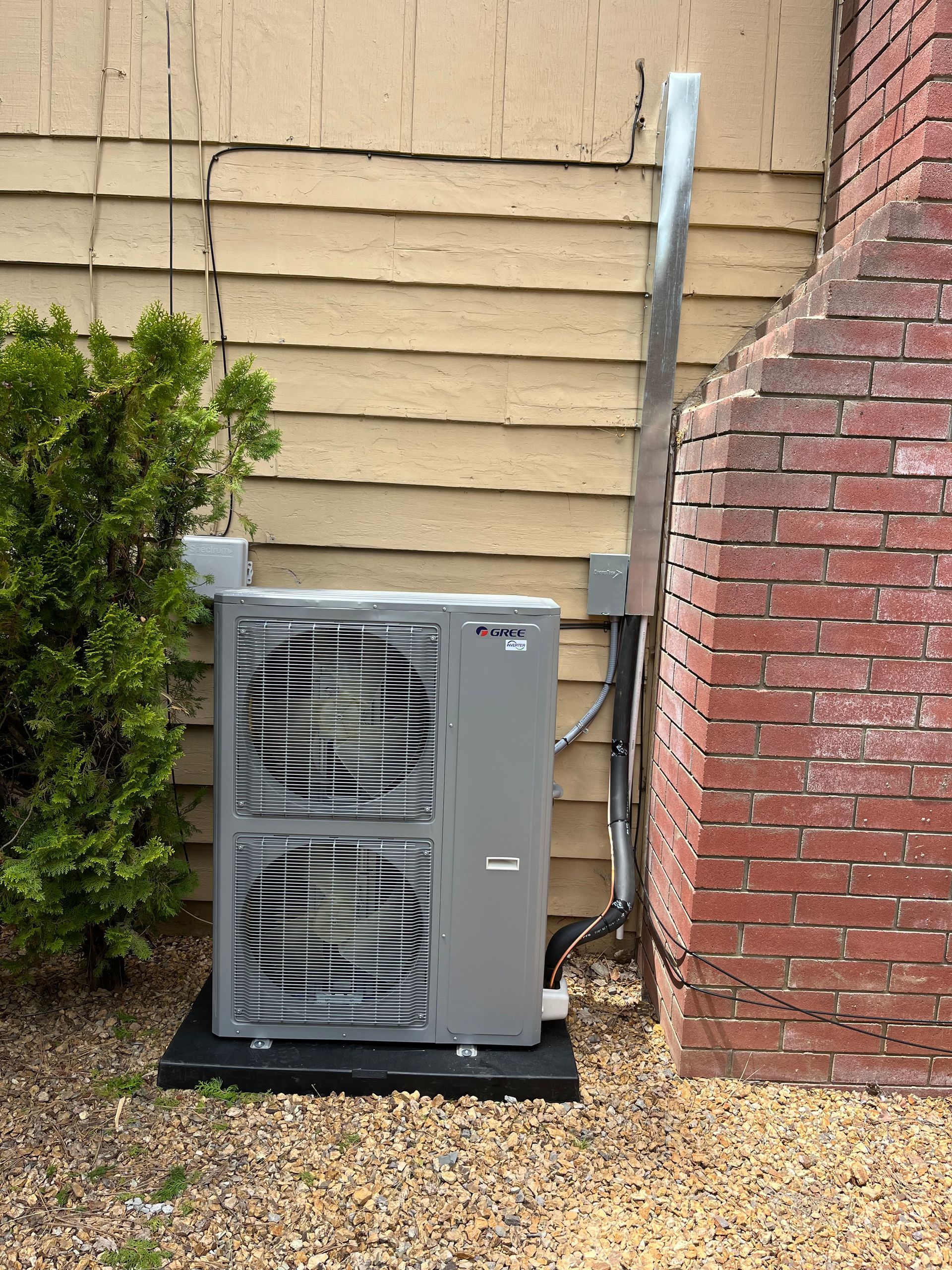 An outdoor air conditioning unit next to a yellow siding wall and a red brick chimney.