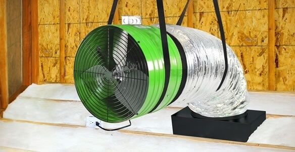A green fan is sitting on top of a wooden table next to a duct.