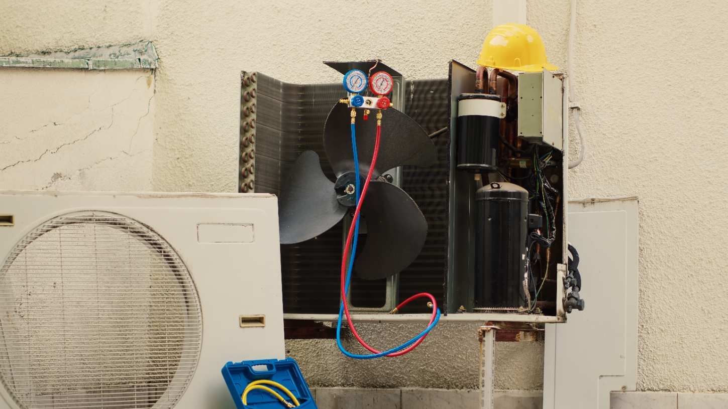 Technician servicing outdoor air conditioner unit with tools beside a house