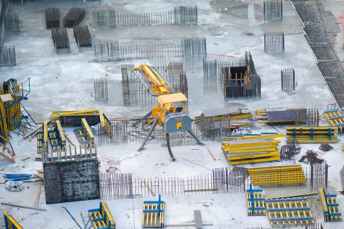 Aerial view of a construction site with a yellow concrete placer pump surrounded by metal rebar and yellow formwork.