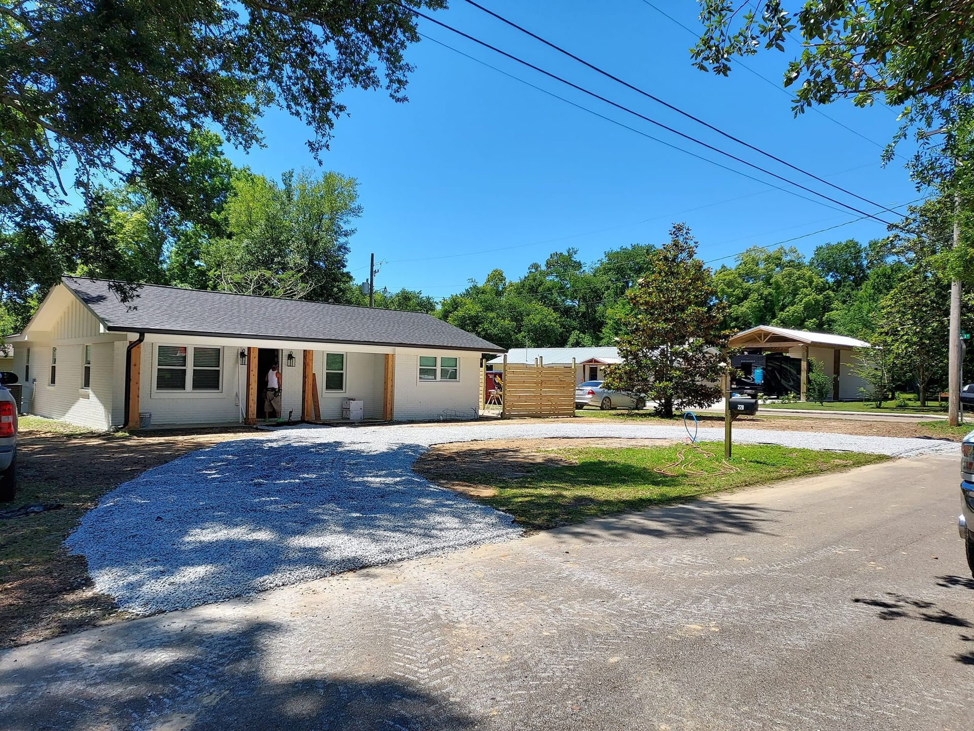 A light-colored house with gravel driveway; two other buildings visible behind it; sunny day.