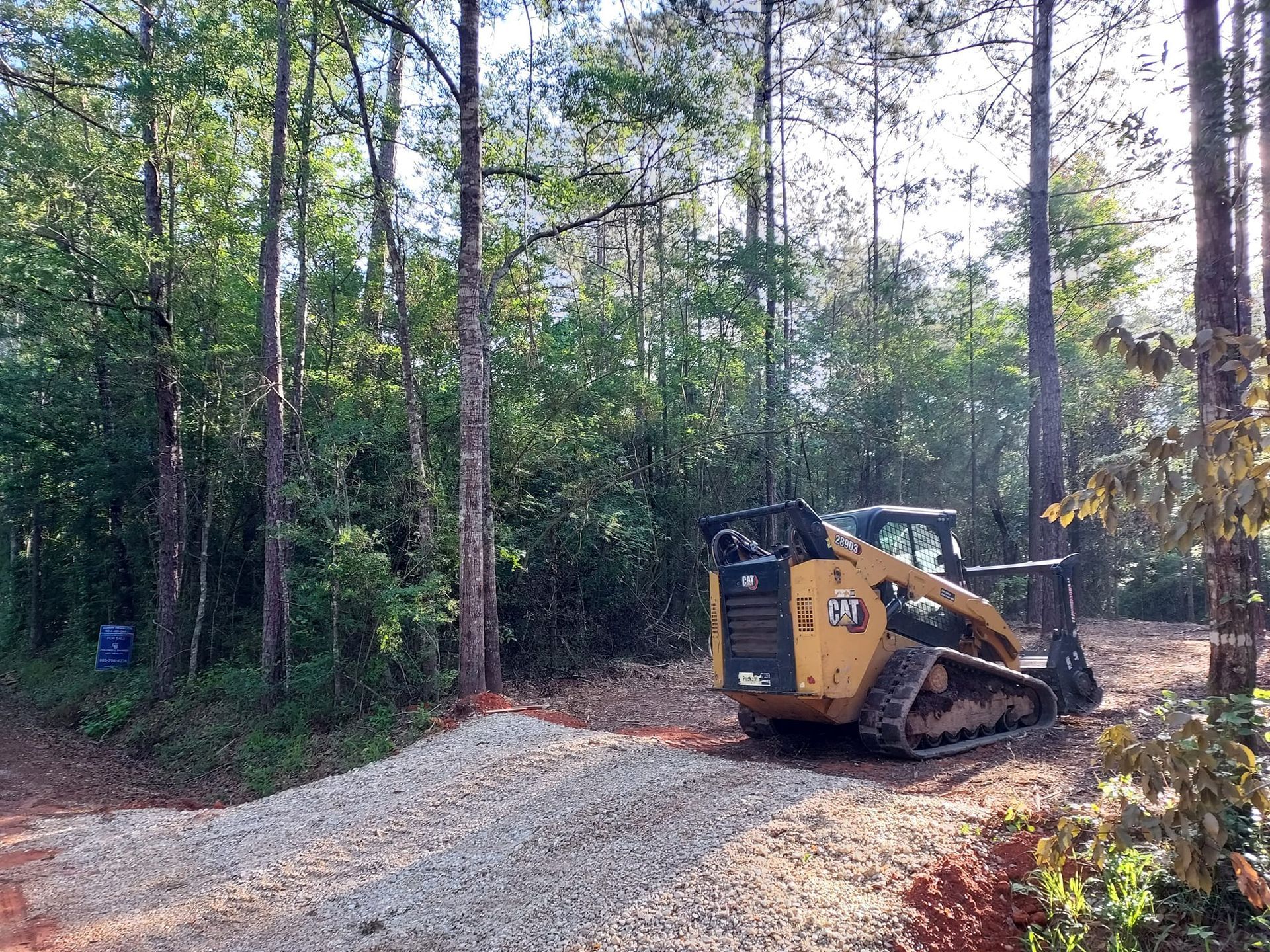 A yellow skid steer on a gravel road, clearing a wooded area.