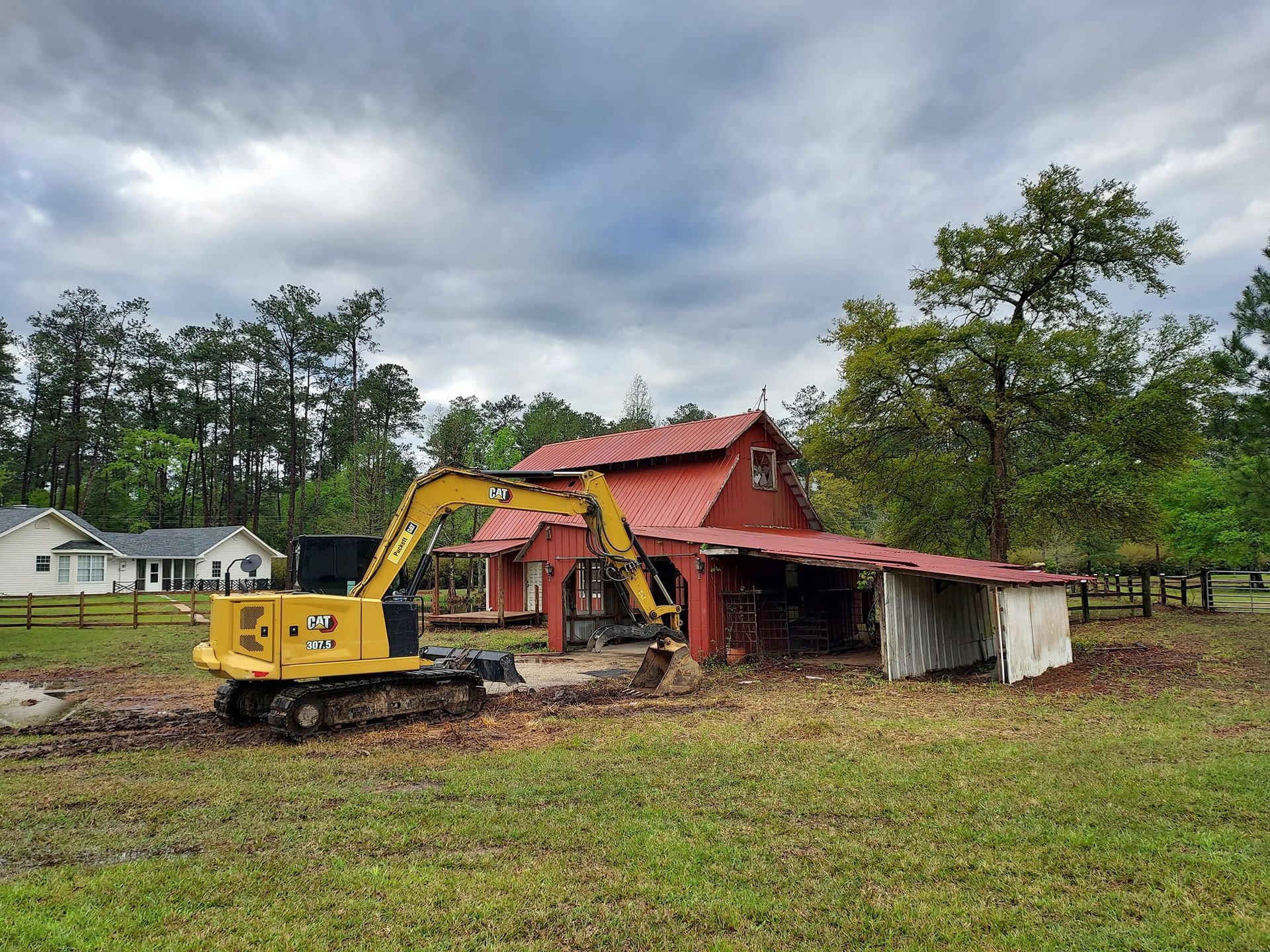 Yellow excavator demolishing a red barn under a cloudy sky; rural setting.