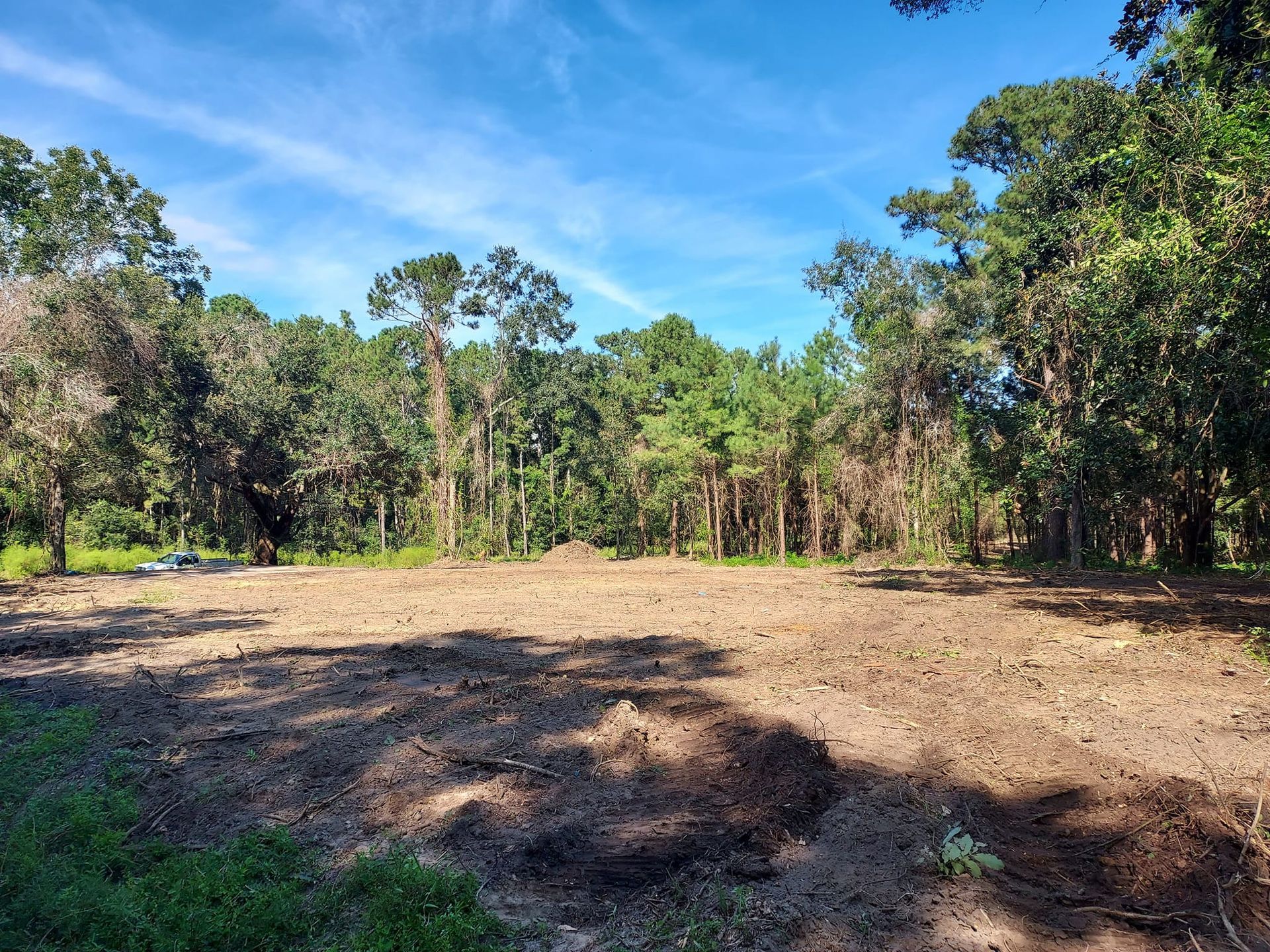 Cleared dirt field with forest backdrop under blue sky.