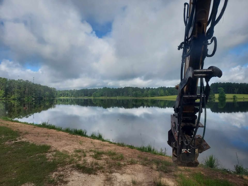 Lakeside view with cloudy sky and a heavy equipment arm in the foreground. Reflection on the water.