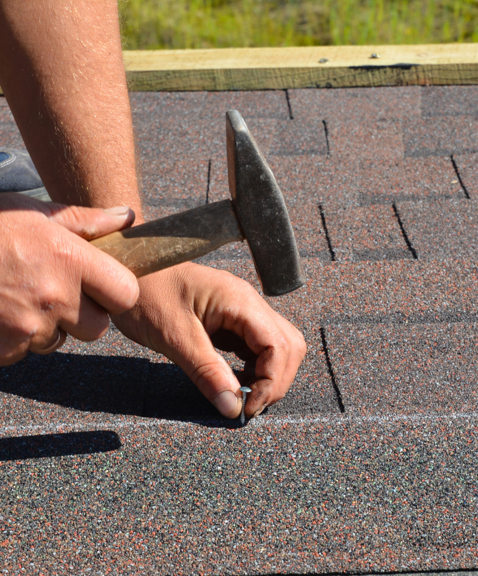 male hands using hammer and nails to nail in roof shingle