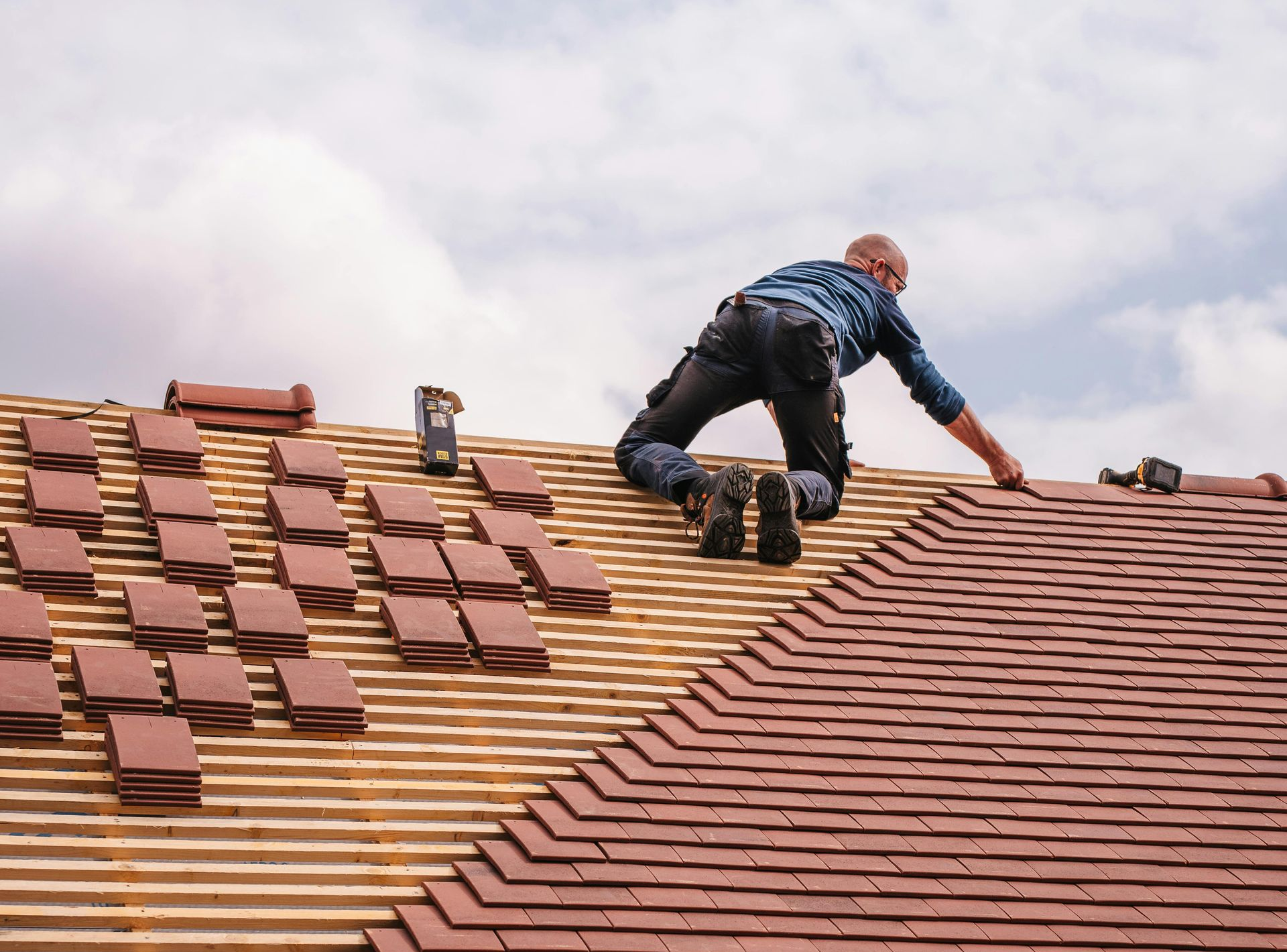 man kneeling on roof laying new tiles