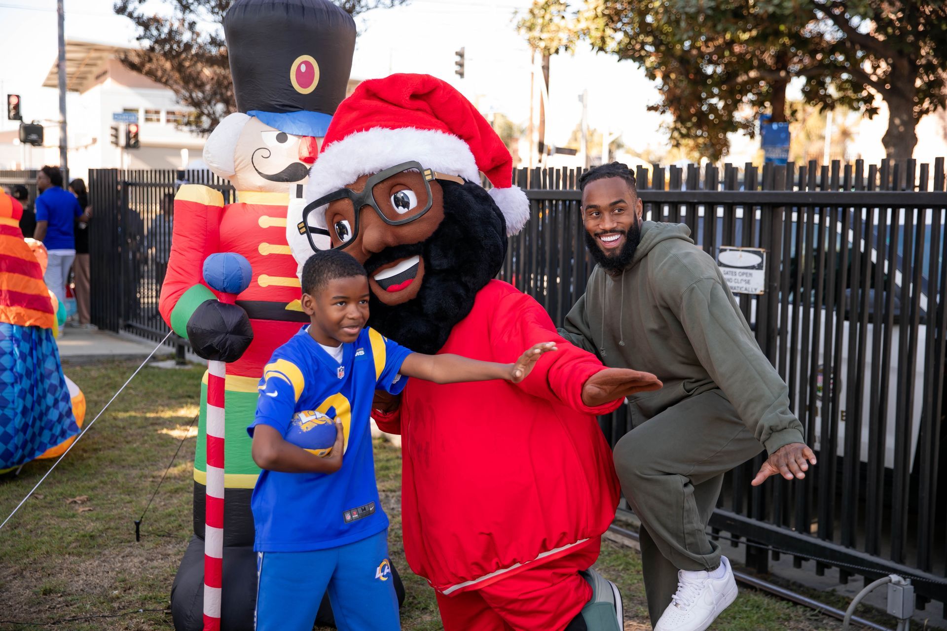 John Johnson III, mascot in Santa hat, boy in Rams gear pose with inflatable nutcracker, outside.