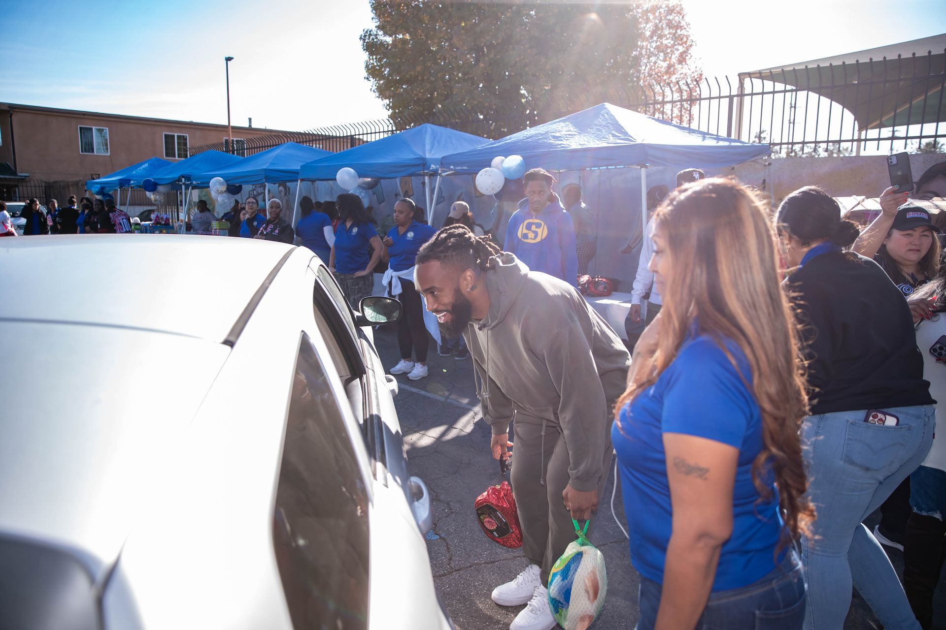 John Johnson III in a grey sweatsuit bends to see into a silver car. People gather under blue tents.