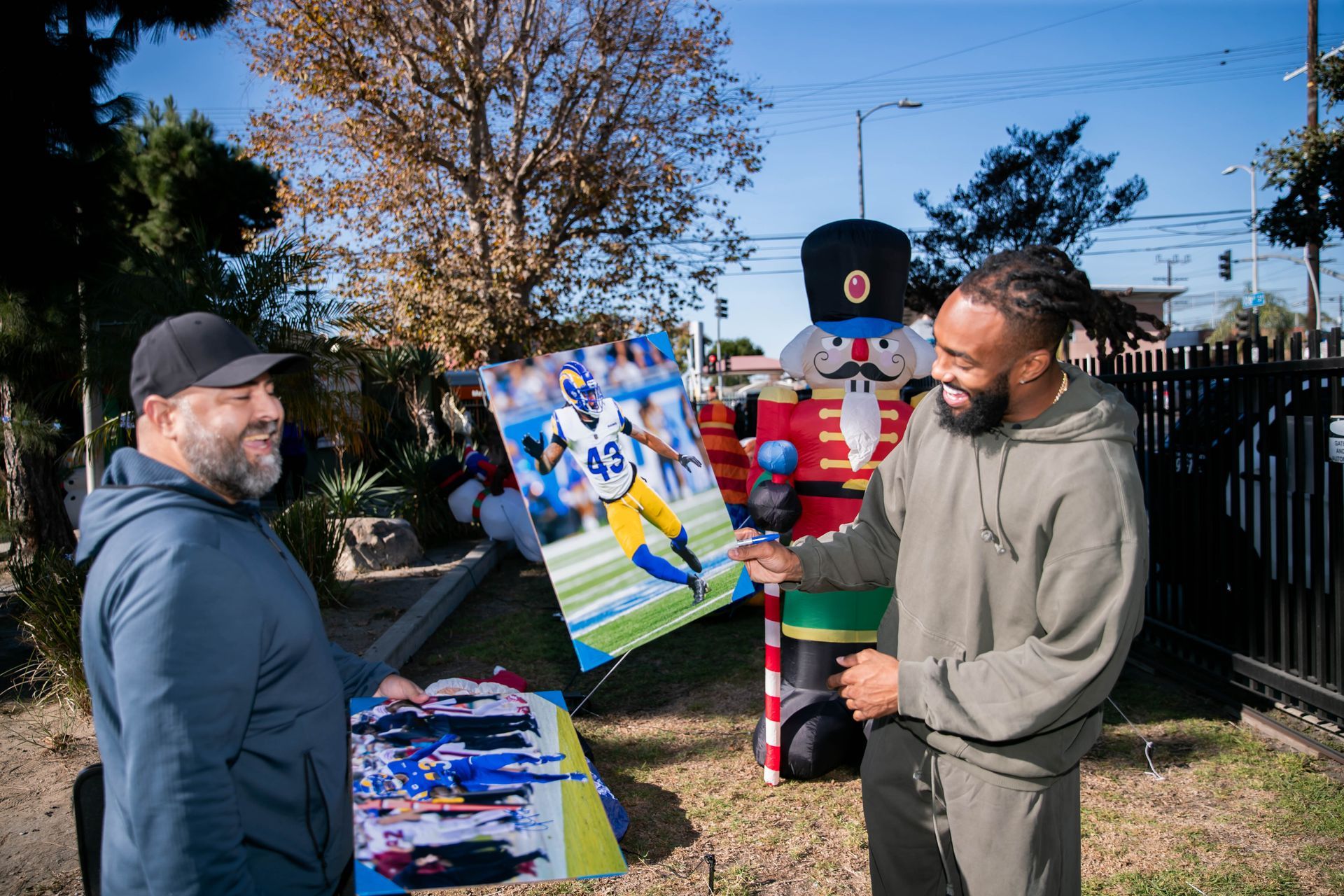 Two men holding artwork of a football player in front of a giant nutcracker decoration. John Johnson III Holiday Giveaway.