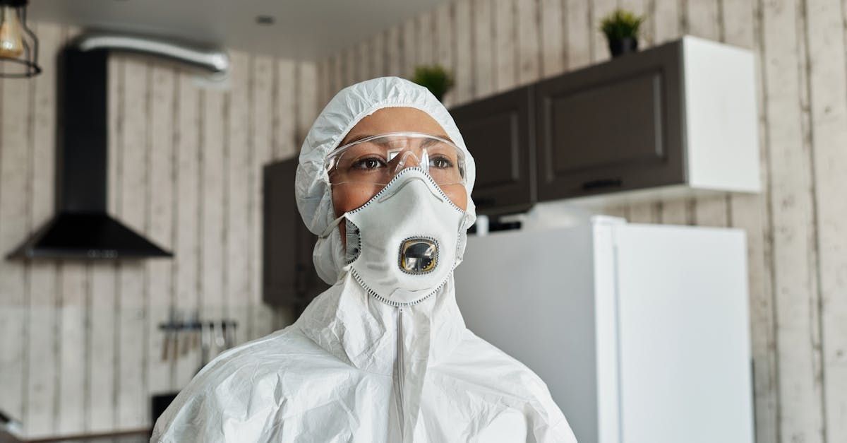 Person in protective suit spraying inside a kitchen cabinet.