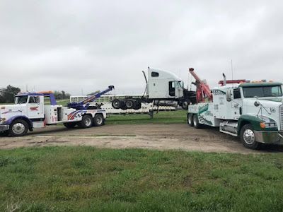 A tow truck is towing a semi truck in a field.