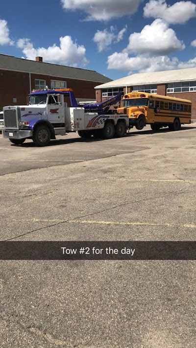A tow truck is towing a school bus in a parking lot.