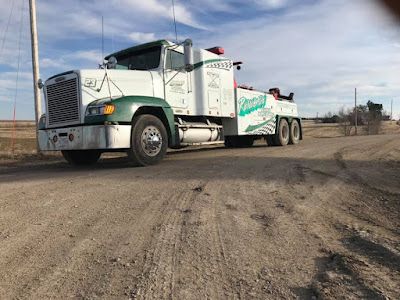 A tow truck is parked on the side of a dirt road.