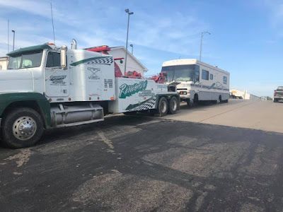 A tow truck is towing a rv down a road.
