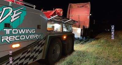 A towing recovery truck is towing a truck in a field at night.